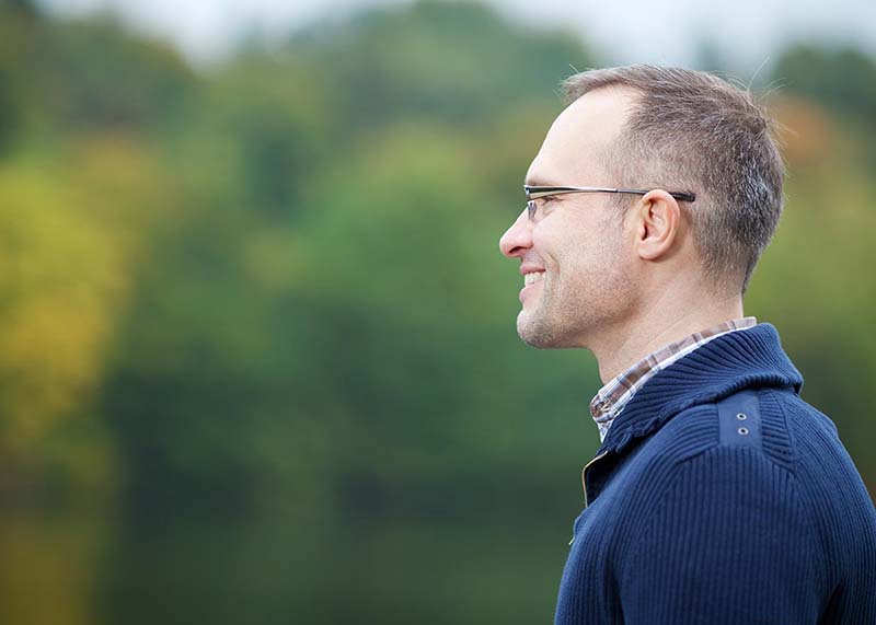 A man with a neck lift stands outdoors while wearing a nice, blue sweater.