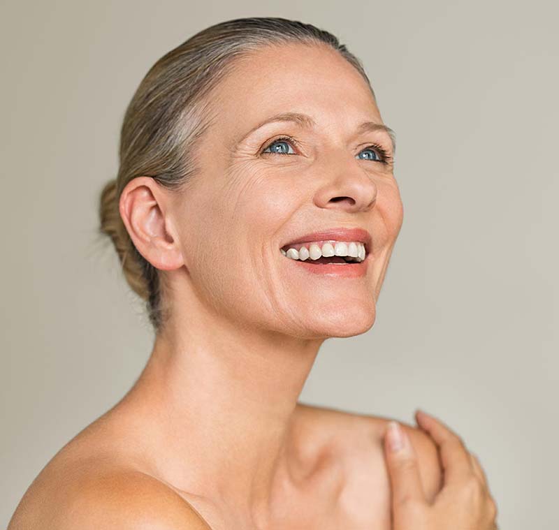 After a facelift, a happy woman smiles widely for a photograph.