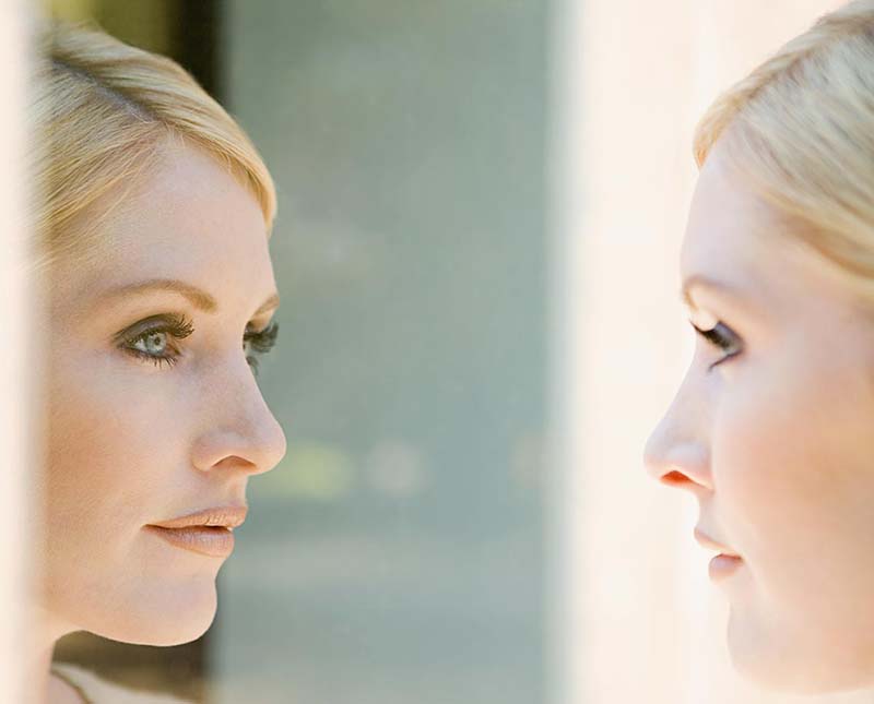 A woman looks at her reflection in the mirror after a neck lift.